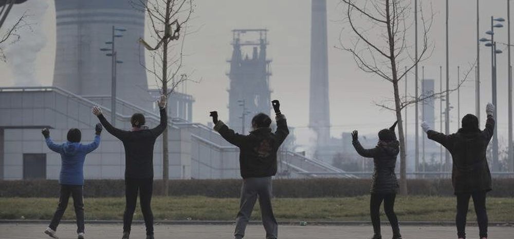 Fotografía facilitada por Greenpeace, de gente haciendo ejercicio frente a chimeneas de industrias en Pekín.