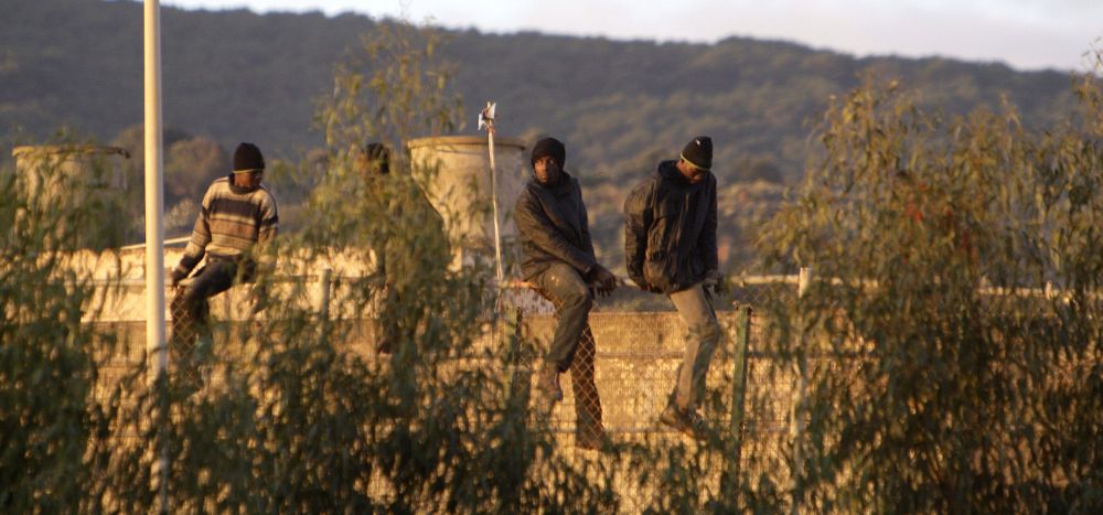 Inmigrantes de origen subsahariano encaramados en lo alto de la verja de Melilla.