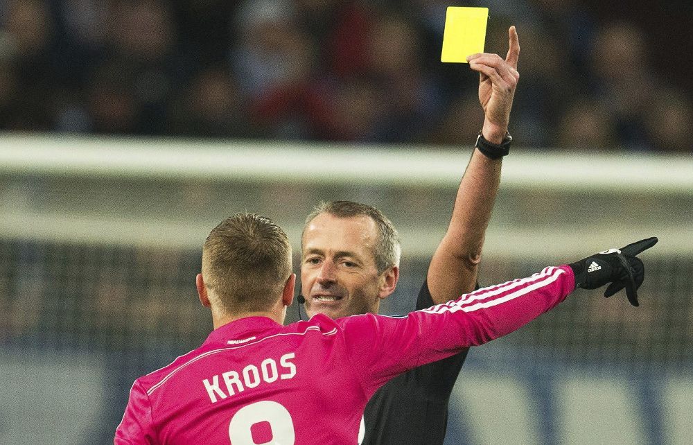El árbitro inglés Martin Atkinson (atrás) muestra la cartulina amarilla al centrocampista alemán Toni Kroos (frente) del Real Madrid durante el partido ante el Shalke 04 de ida de dieciseisavos de final de la Liga de Campeones contra el Schalke 04 en Gelsenkirchen.