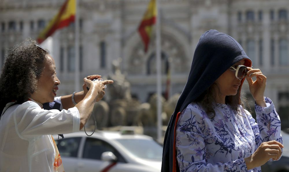 Turistas hoy, en Madrid, protegiéndose del calor..