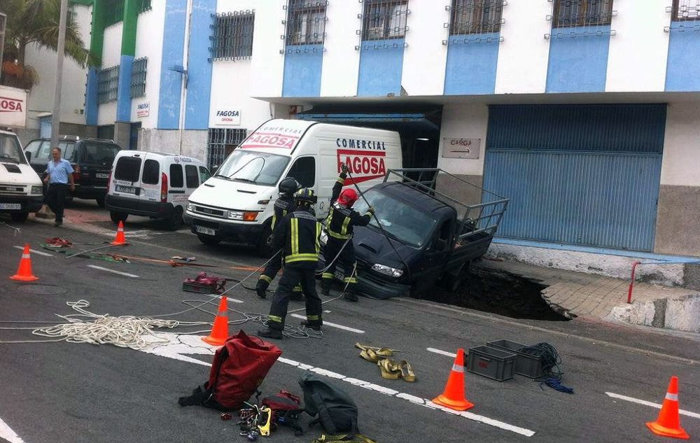 Fotografía facilitada por la Policía Local de Las Palmas de Gran Canaria, del rescate por los bomberos de un hombre que se ha quedado atrapado tras ser engullido su coche por un socavón en la calle Artenara.