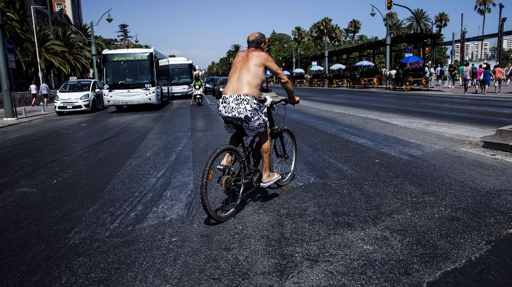 Un hombre en bañador circula en bicicleta por el centro de Málaga, hoy donde los termómetros marcan 35º.