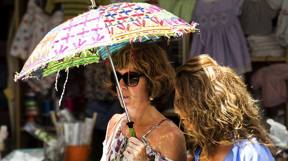 Dos mujeres se protegen del intenso sol bajo un paraguas.
