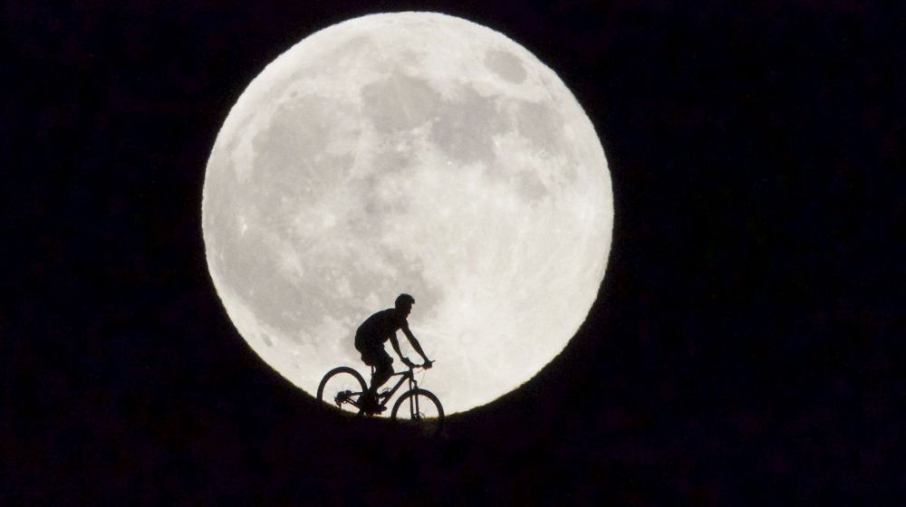 Un ciclista pasa delante de la Luna llena que se observó en la isla de Fuerteventura.