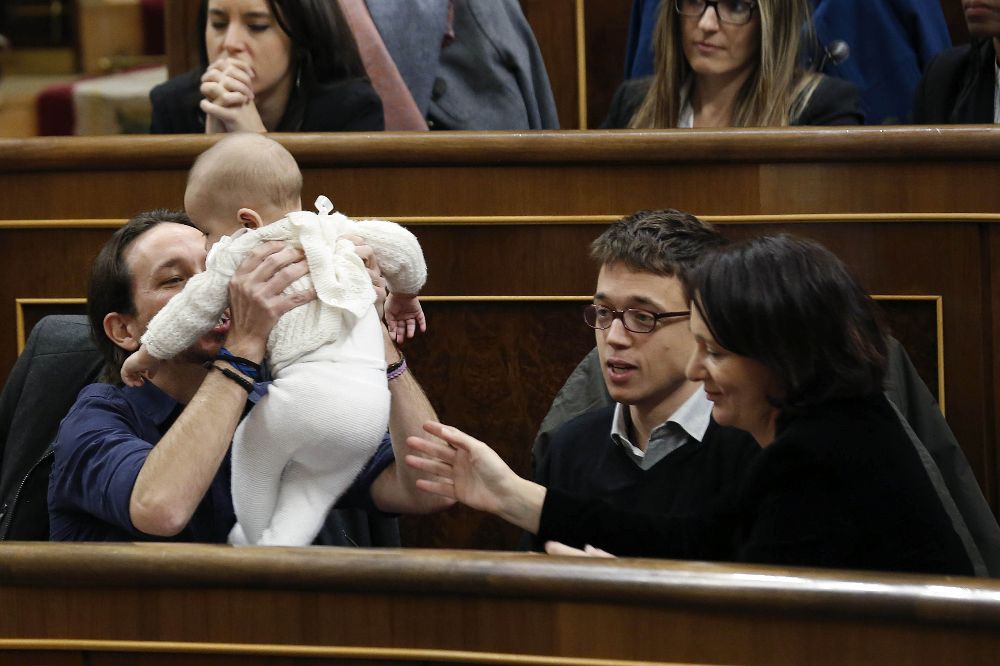 El líder de Podemos, Pablo Iglesias (i), coge a la hija de la diputada de su partido Carolina Bescansa, en presencia del diputado íñigo Errejón, en el hemiciclo del Congreso.