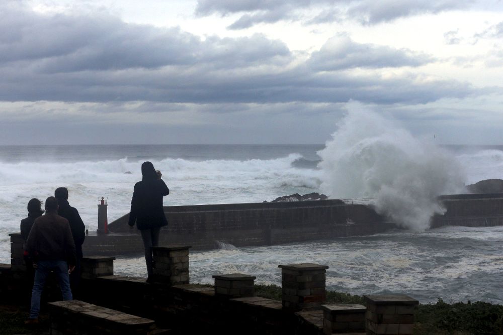 Varias personas contemplan las olas esta tarde en la entrada del puerto de Tapia de Casariego, en el occidente de Asturias.