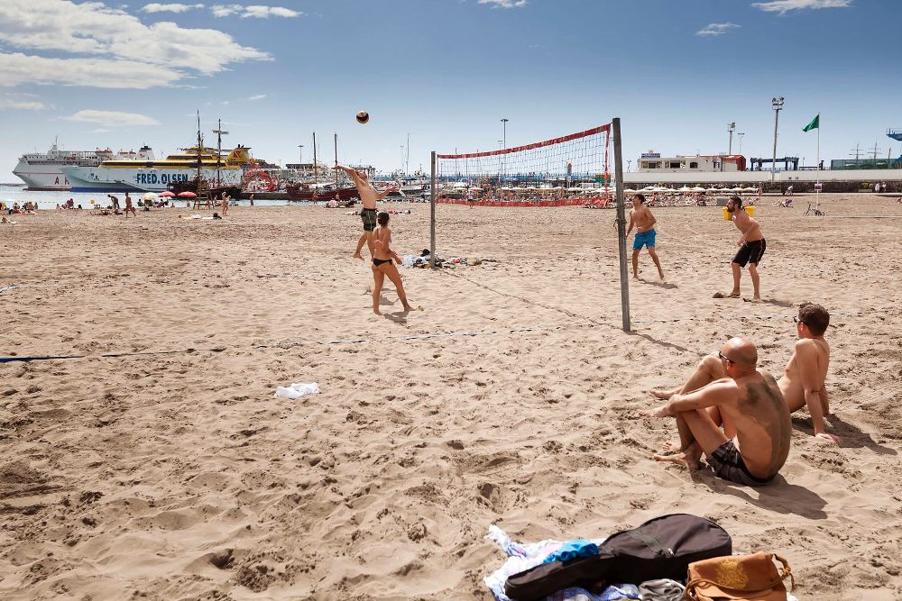 Varias personas disfrutan de las agradables temperaturas en la playa de Los Cristianos, en Arona.