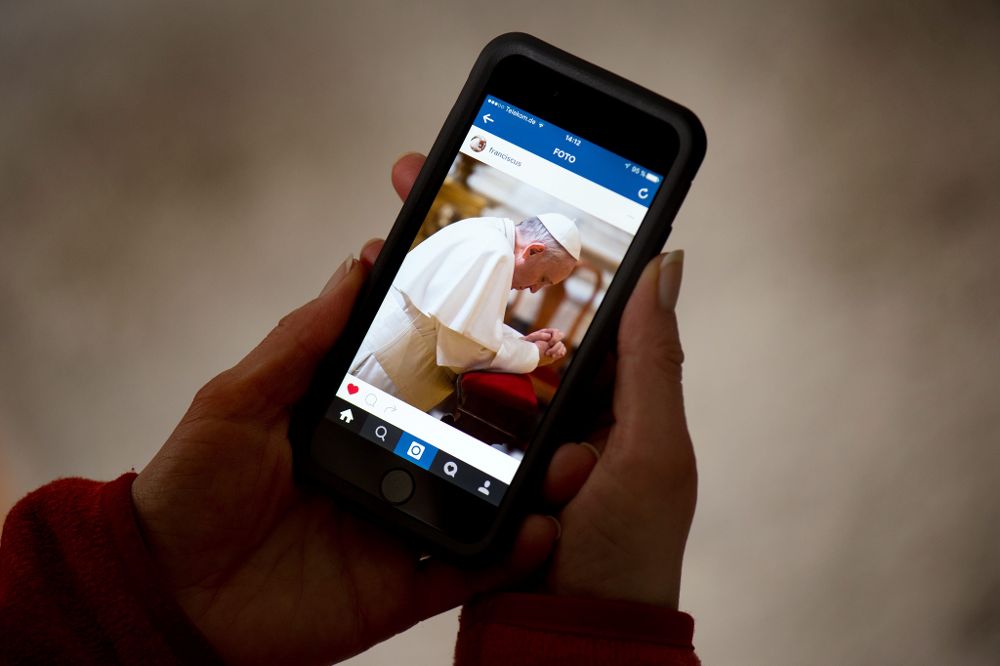 Una mujer alemana sujera un smartphone que muestra una foto del papa en Instagram. 
