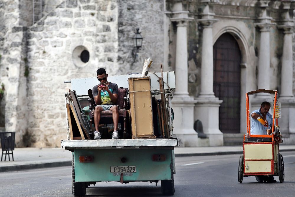 Un hombre juega con su teléfono móvil mientras viaja en la parte trasera de un camión en La Habana.