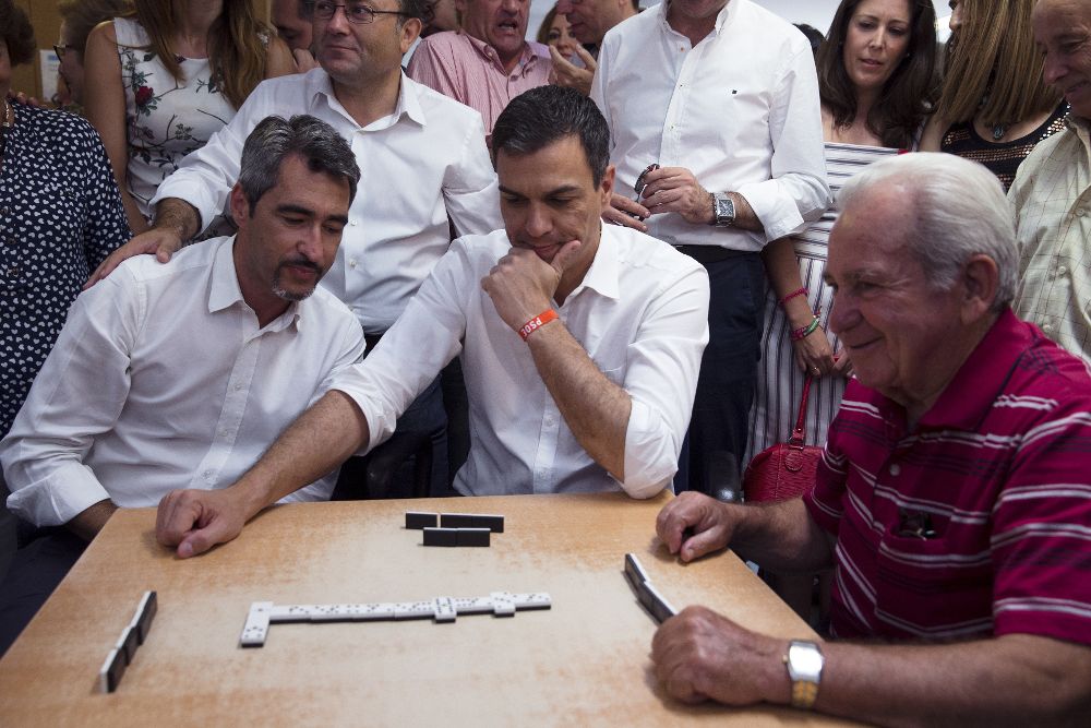 El líder del PSOE y candidato a la presidencia del Gobierno, Pedro Sánchez (c), durante una partida de dominó que ha jugado hoy con los mayores del centro de Anica Torres de Benalmádena (Málaga), junto al alcalde de dicho municipio, Víctor Navas (i).