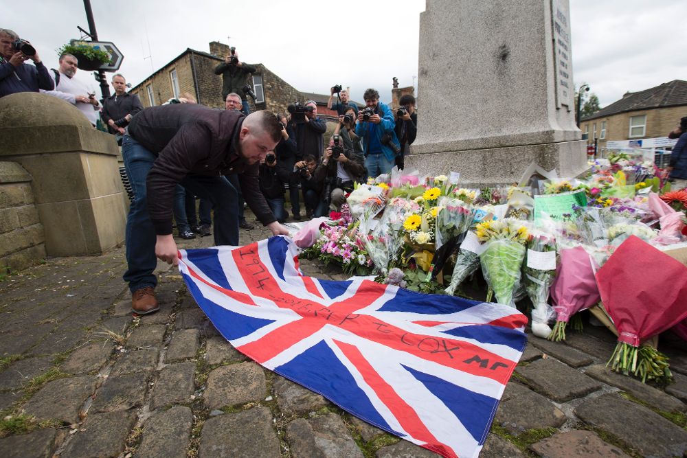 Un hombre coloca una bandera del Reino Unido junto a flores y mensajes de condolencias colocados cerca del lugar donde se produjo ayer el asesinato de la diputada laborista Jo Cox.