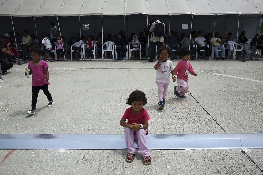Varios niños juegan mientras un grupo de refugiados y migrantes esperan para el proceso de pre-registro en un campamento de refugiados situado en el antiguo aeropuerto de Helliniko de Atenas.