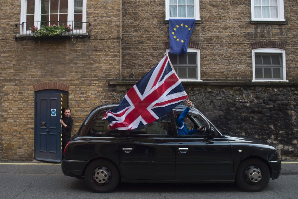 Un taxista londinense ondea una bandera británica mientras circula por una calle donde una bandera europea ondea en una ventana en Londres.