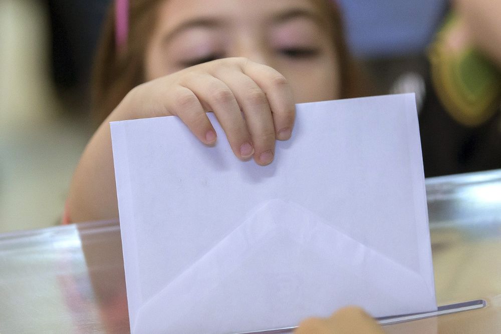 Una niña intenta introducir el sobre en la urna con el voto de su madre.