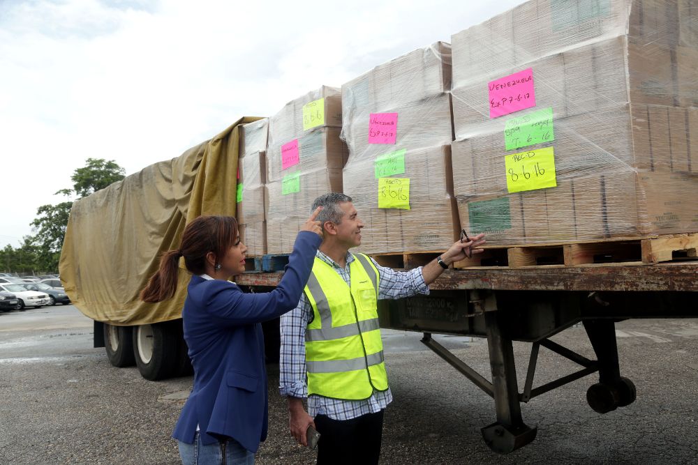 El viceministro de Comercio Interior de Venezuela y la embajadora del país en Trinidad y Tobago examinan la carga de 170 toneladas de alimentos que fue enviada desde este último país en avión hacia Venezuela el 23 de junio.