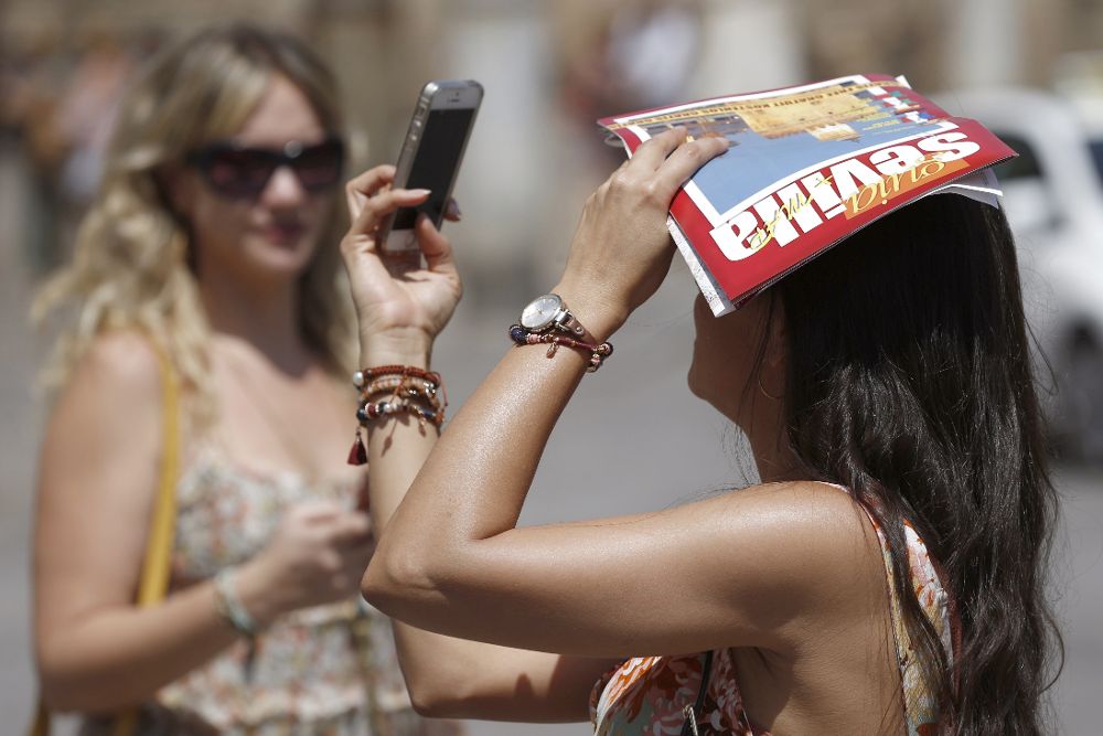 Una turista se fotografía mientras se proteje del sol con una guía turística de Sevilla.