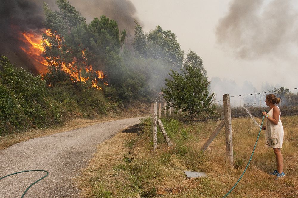 Una mujer observa cómo llegan a las casas de la zona de Sela las llamas del incendio forestal de Arbo (Pontevedra), en el que se ha decretado la Situación 2, por la cercanía del fuego a núcleos de población. 