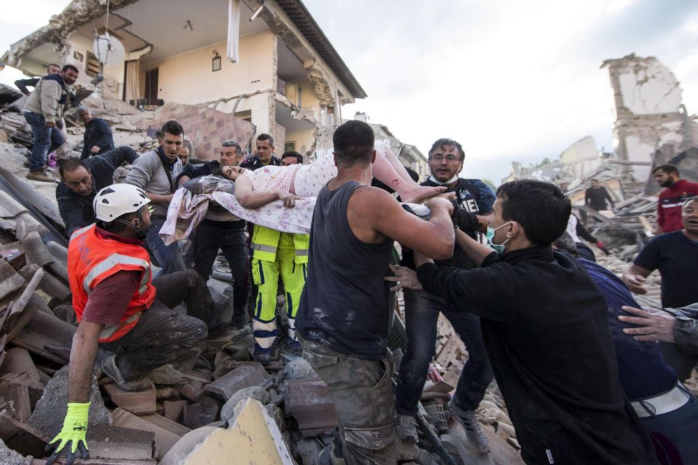 Una mujer herida (c) es rescatada de entre los escombros de un edificio en Amatrice, en el centro de Italia.