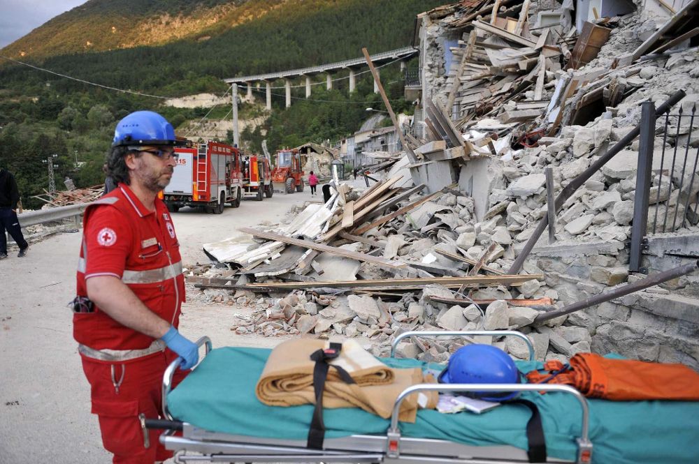 Un trabajador de la Cruz Roja italiana lleva una camilla delante de los escombros de un edificio en Pescara del Tronto, cerca de la localidad de Arquata del Tronto, en la provincia de Ascoli Piceno.