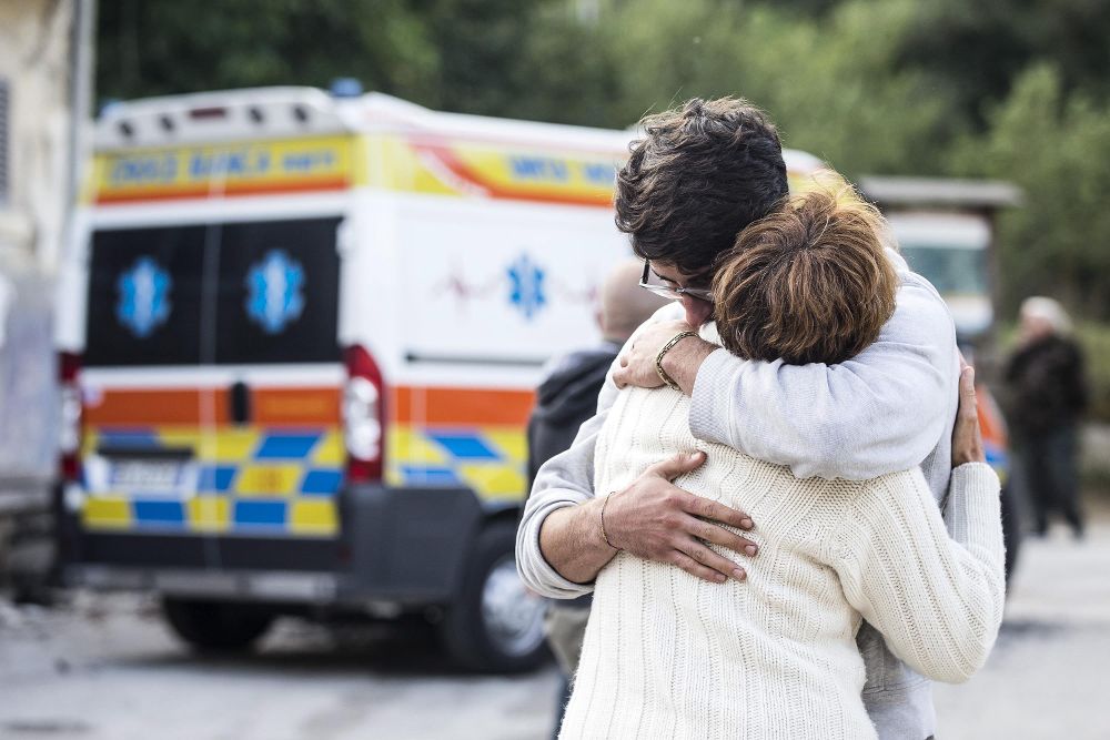Dos personas se abrazan junto a una ambulancia.