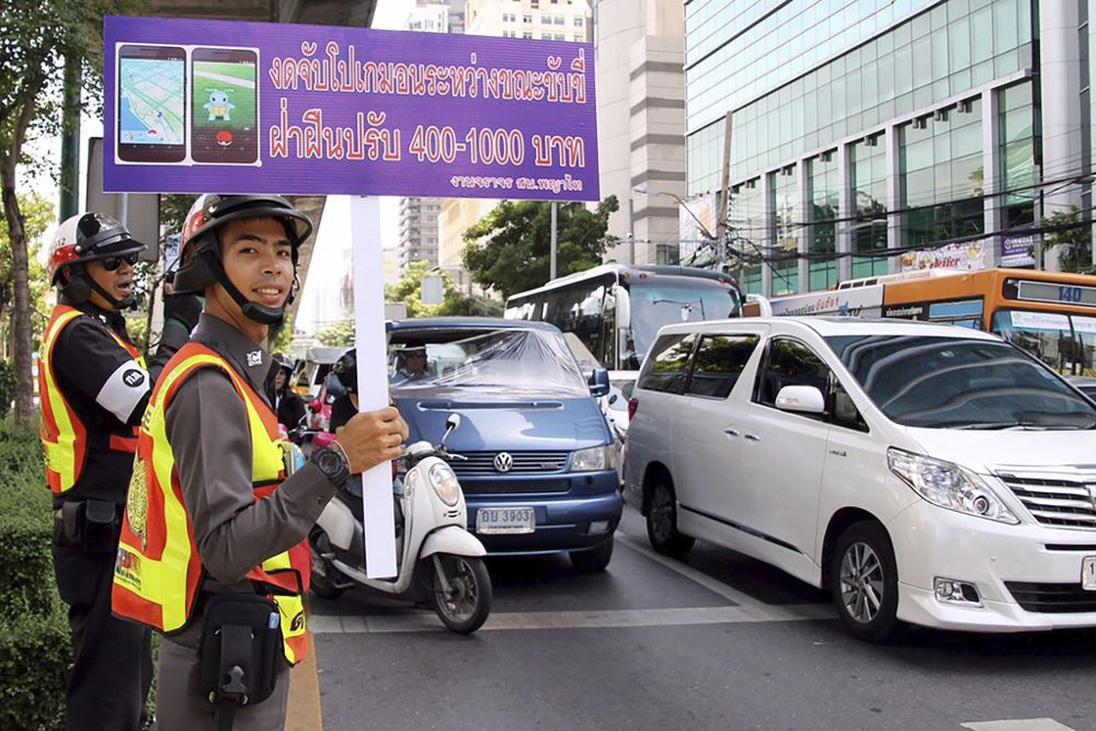 Un guardia de tráfico sostiene una pancarta en la que se lee "No juege a Pokemon Go mientras conduce, los infractores serán multados" en Tailandia.