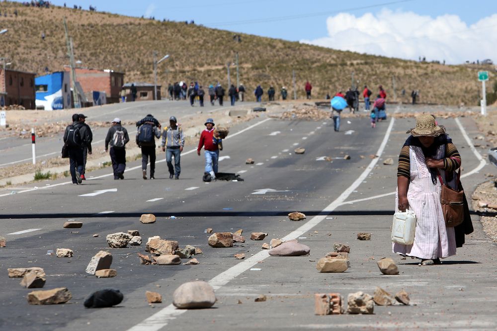 Ciudadanos bolivianos caminan por una vía bloqueada por mineros de las cooperativas que protestan.