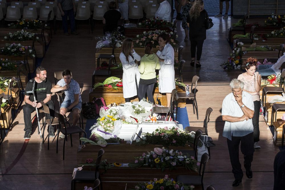 Varias personas entre los féretros poco antes del funeral multitudinario por las víctimas en Ascoli Piceno, en la región de Marche.