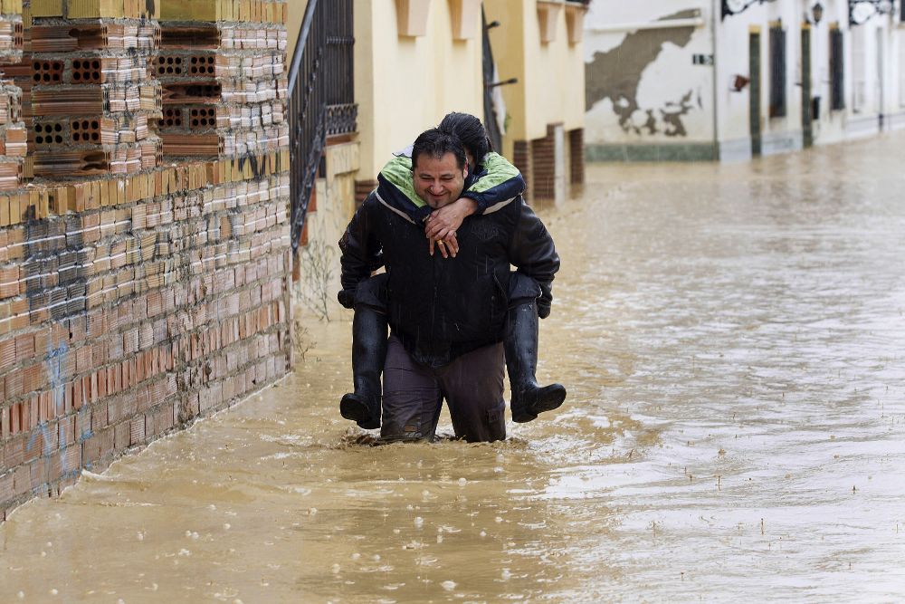 Una persona camina con otra a hombros entre las casas inundadas en la barriada Doña Ana de la localidad de Cártama (Málaga).