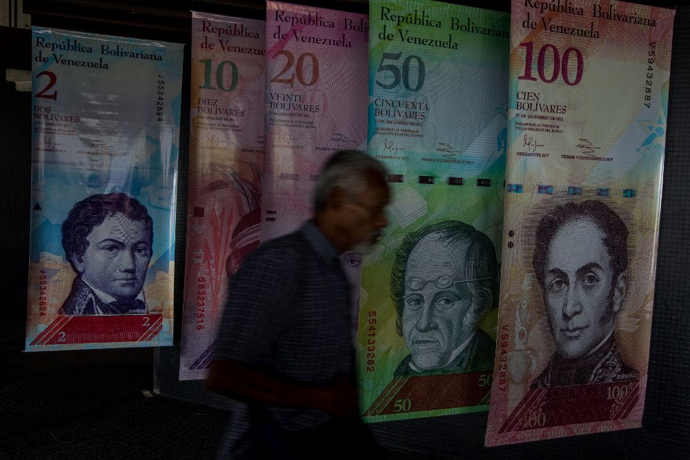 Un hombre camina frente a carteles con la imagen de billetes venezolanos en el Banco Central de Venezuela.