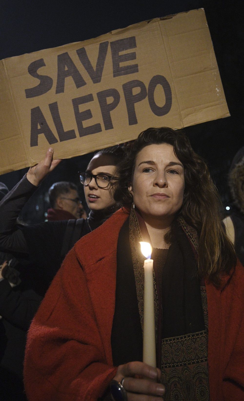 Vista de dos manifestantes, uno sosteniendo una vela y otro una pancarta en la que se puede leer 'Salvad a Alepo' durante una manifestación contra los bombardeos en Alepo y el papel de Siria delante del número 10 de Downing Street en Londres, Reino Unido.