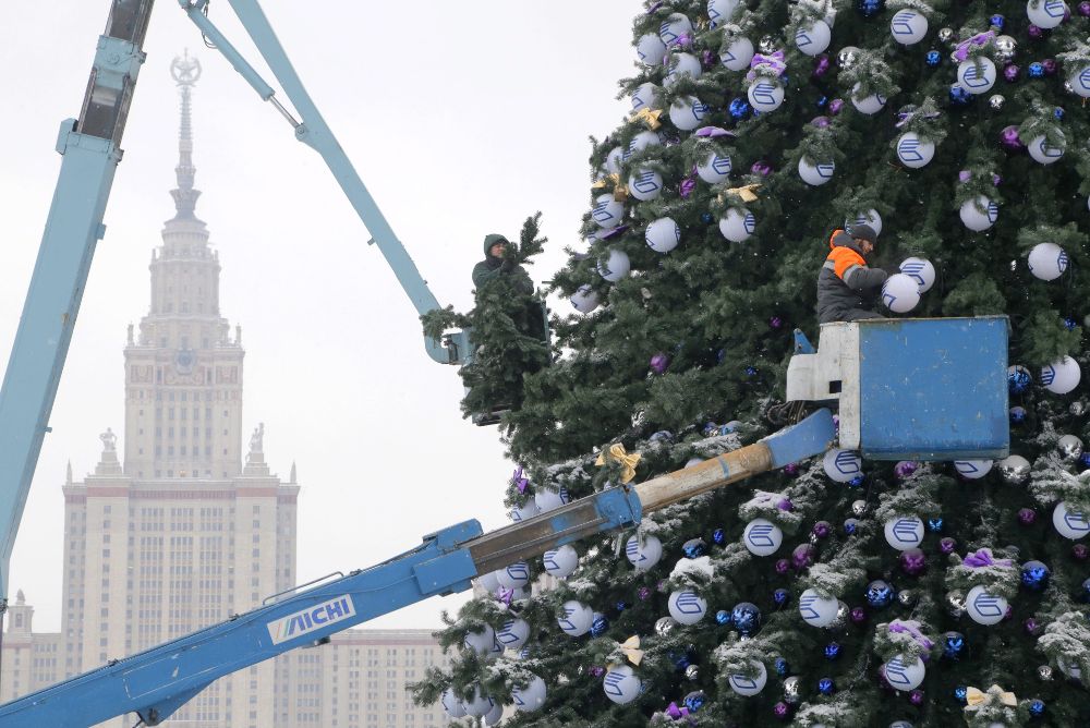 Unos trabajadores decoran un árbol de Navidad frente al edificio de la Universidad de Moscú durante una nevada en Moscú.