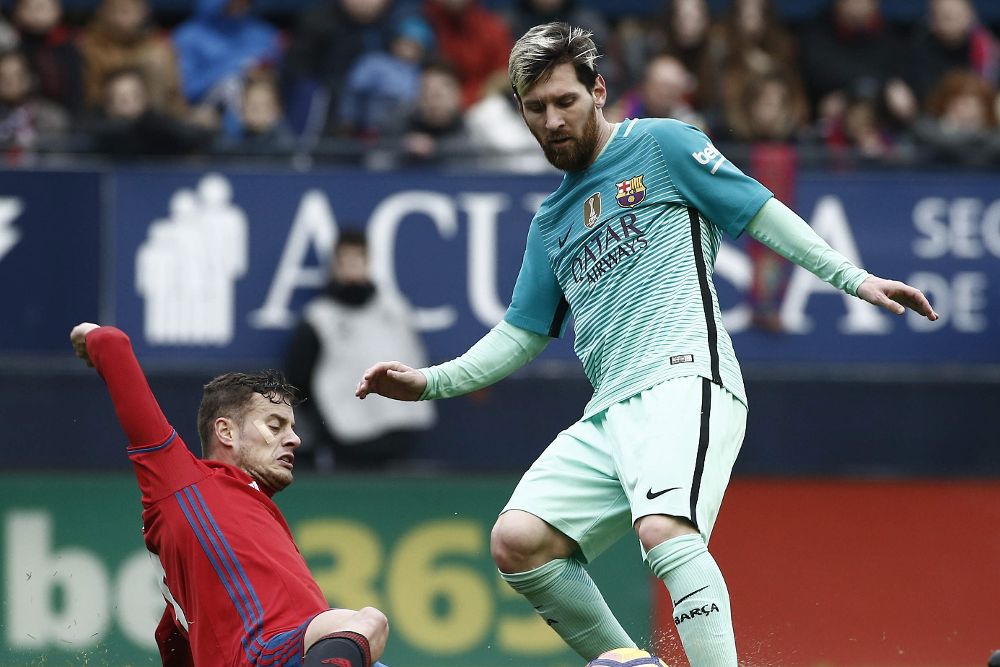 El delantero de Osasuna Oriol Riera (i) se lanza a los pies del delantero argentino del F.C Barcelona Leo Messi.