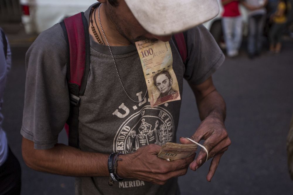 Un hombre organiza sus billetes de 100 bolívares mientras hace fila en las inmediaciones del Banco Central de Venezuela.