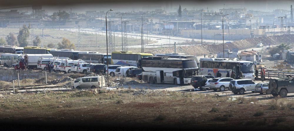 Unos autobuses esperan para transportar a un grupo de combatientes opositores.