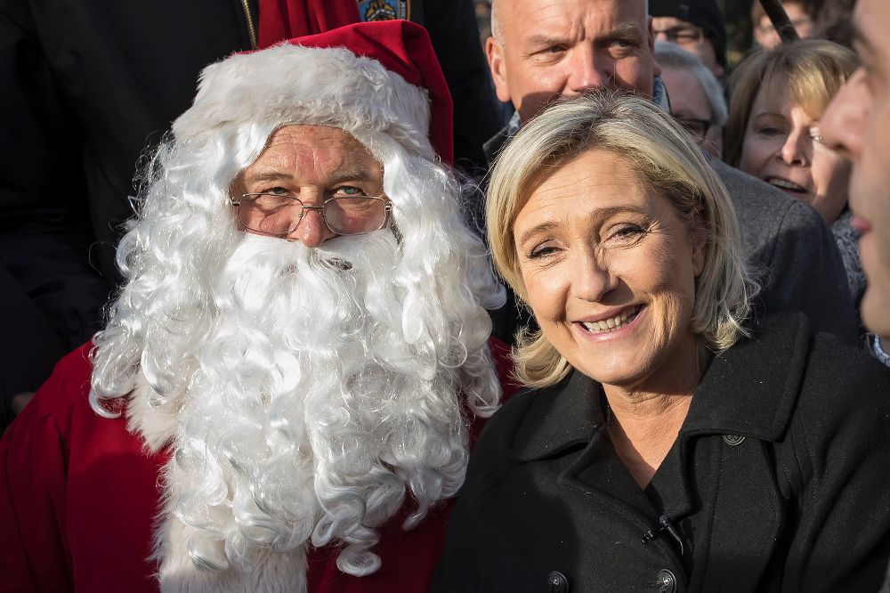 La líder del ultraderechista Frente Nacional francés, Marine Le Pen, posa junto a un papá noel durante una visita a un mercado navideño en los Campos Elíseos en París.