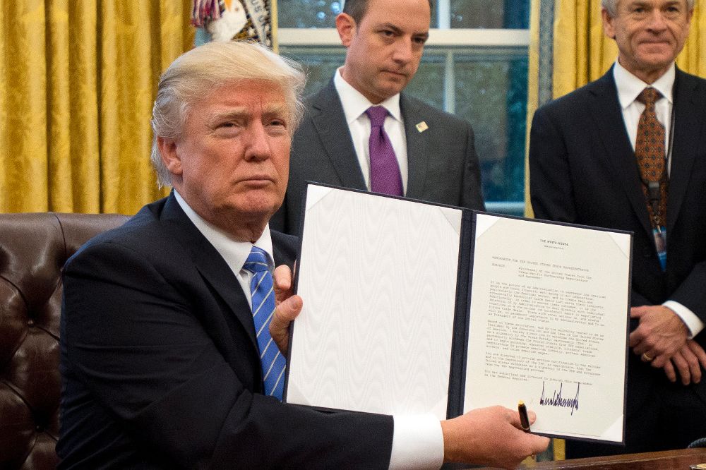 El presidente estadounidense, Donald Trump (c), muestra la orden ejecutiva para sacar a EE.UU. del acuerdo comercial TPP (Acuerdo de Asociación Transpacífico), en el Despacho Oval de la Casa Blanca, en Washington, Estados Unidos.