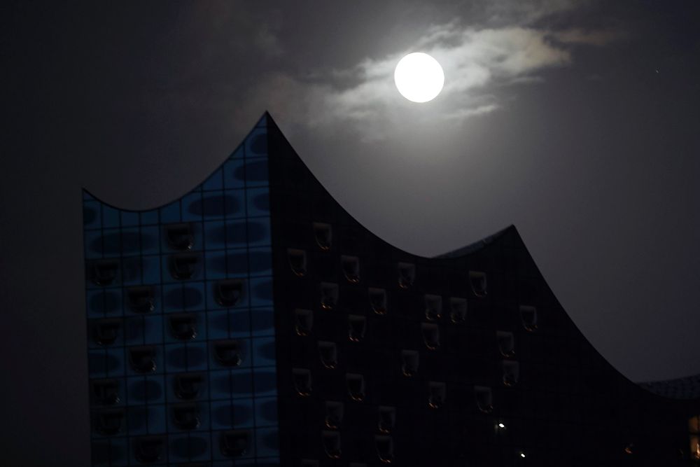 La luna brilla detrás de la sala de música Elphilharmonie, durante una ceremonia de apertura en Hamburgo, (Alemania).