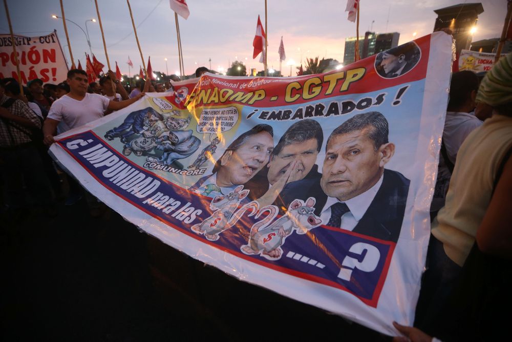 Manifestantes marchan con una pancarta donde aparecen los expresidentes Alejandro Toledo, Alan García y Ollanta Humala, vinculados al escándalo de corrupción de Odebrecht.
