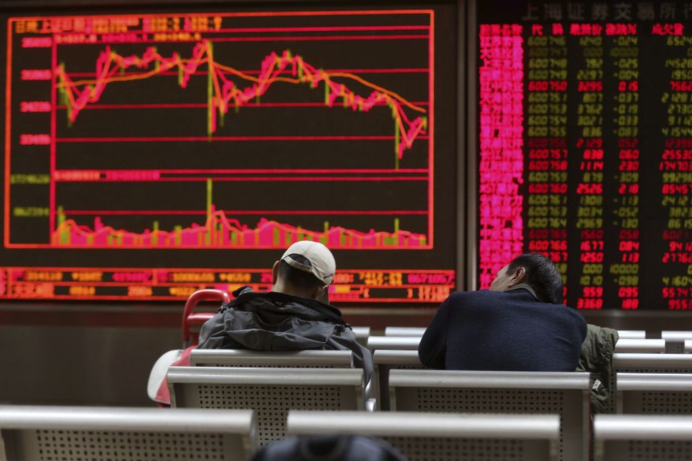 Un par de inversores chinos se echan una siesta delante de varias pantallas que muestran información de la Bolsa de Shanghái.
