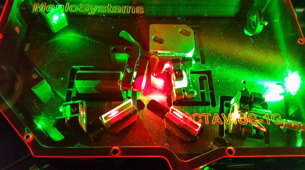 Fotografía del resonador óptico que genera el Astro Laser Frequency Comb. La luz verde procede del bombeo óptico que se utiliza como fuente de energía y la luz roja es el propio peine láser, que se origina en un pequeño cristal de zafiro dopado con titanio (zona brillante en el centro de la foto). La cavidad está formada por cuatro espejos que confinan la trayectoria del láser y otros elementos ópticos correctores.