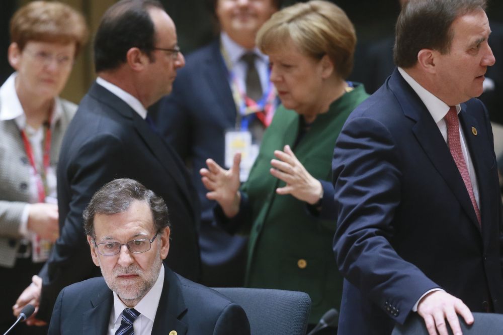 Mariano Rajoy aguarda sentado mientras la canciller alemana, Angela Merkel y el presidente de Francia, François Hollande (detrás), charlan durante una reunión celebrada en el marco de la cumbre de primavera de los líderes de la Unión Europea.