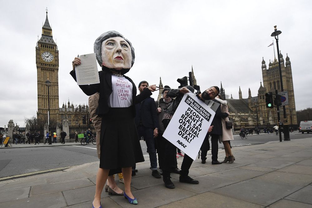 Una manifestante disfrazada de la primera ministra británica, Theresa May (i), posa junto a otros que sostienen una pancarta contra la salida del Reino Unido de la UE.