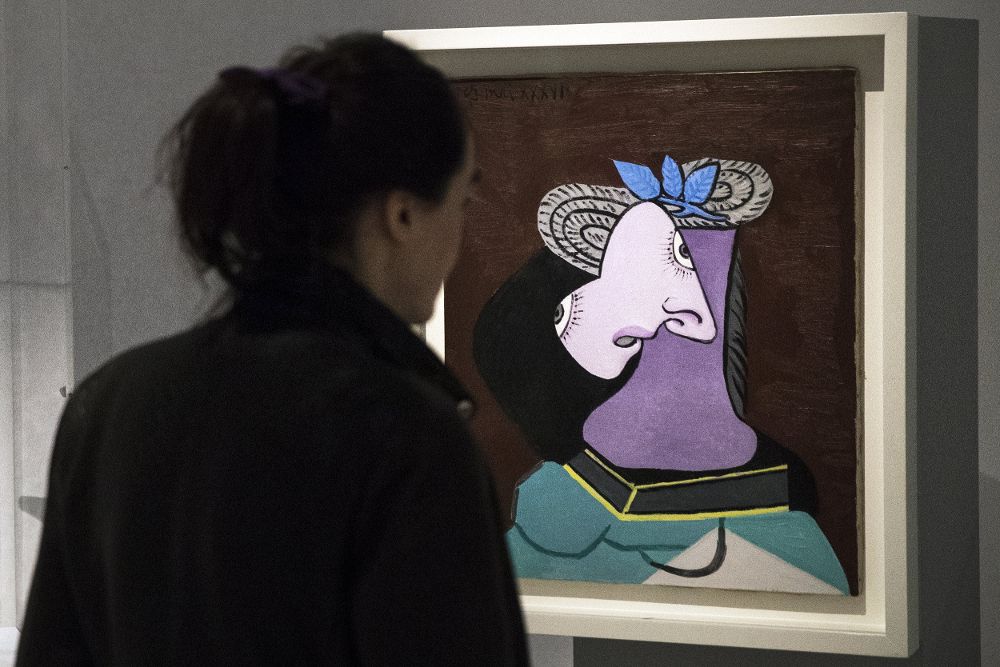 Una mujer observa el cuadro 'Sombrero de paja con hojas azules' del artista español Pablo Picasso.
