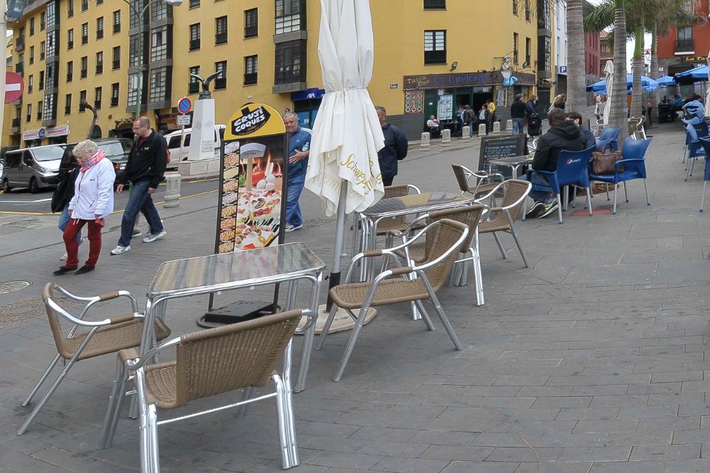 Sillas, mesas y carteles de la terraza de un bar en una calle portuense.