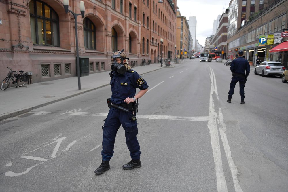 Miembros de la policía sueca se ajustan las máscaras antigas en la zona donde un camión que ha atropellado a varias personas y se ha estrellado contra una tienda de la calle comercial de Drottninggatan en el centro de Estocolmo.