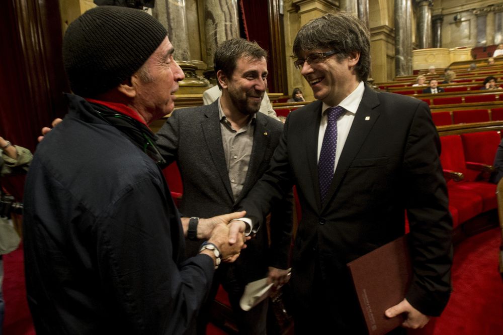 El presidente de la Generalitat de Cataluña, Carles Puigdemont (d), saluda al diputado de JxSí Lluís Llach (i) en presencia del conseller de Salud, Antoni Comín.