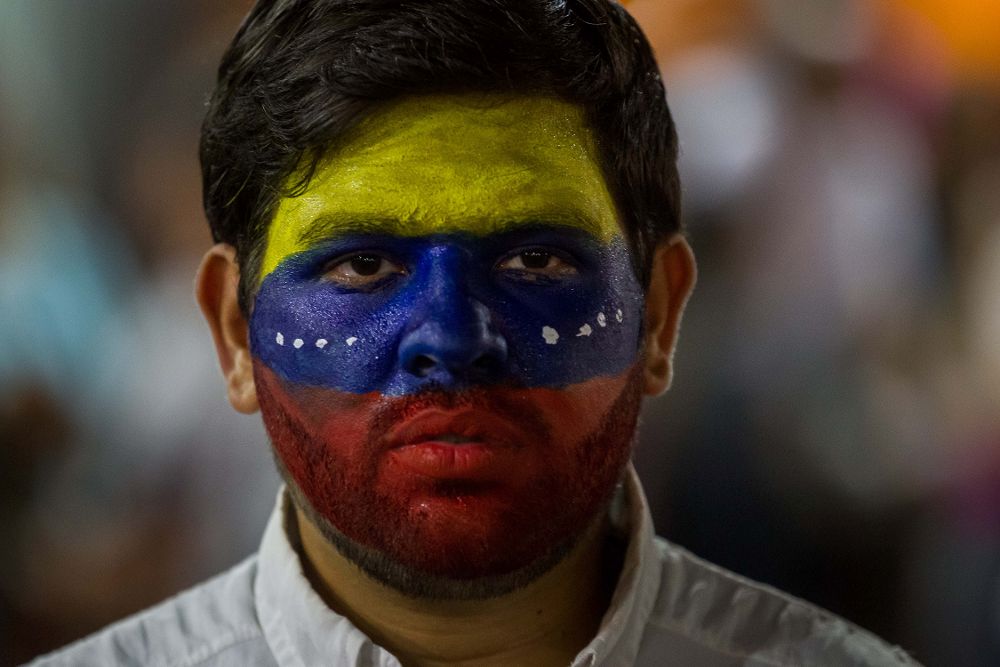 Un hombre con el rostro pintado con los colores de la bandera venezolana.