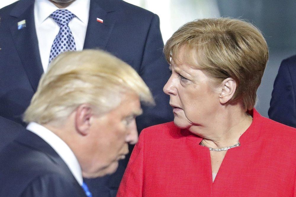 El presidente estadounidense pasa por delante de la canciller alemana, Angela Merkel, durante la foto de familia de los asistentes a la cumbre de la OTAN.