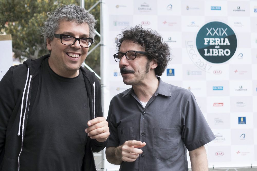 El cantautor tinerfeño Pedro Guerra (i) y Darío Adanti, uno de los fundadores de la revista Mongolia, y autor de 'Disparen al humorista' charlan durante el acto de apertura de la XXIX Feria del Libro de Las Palmas de Gran Canaria.
