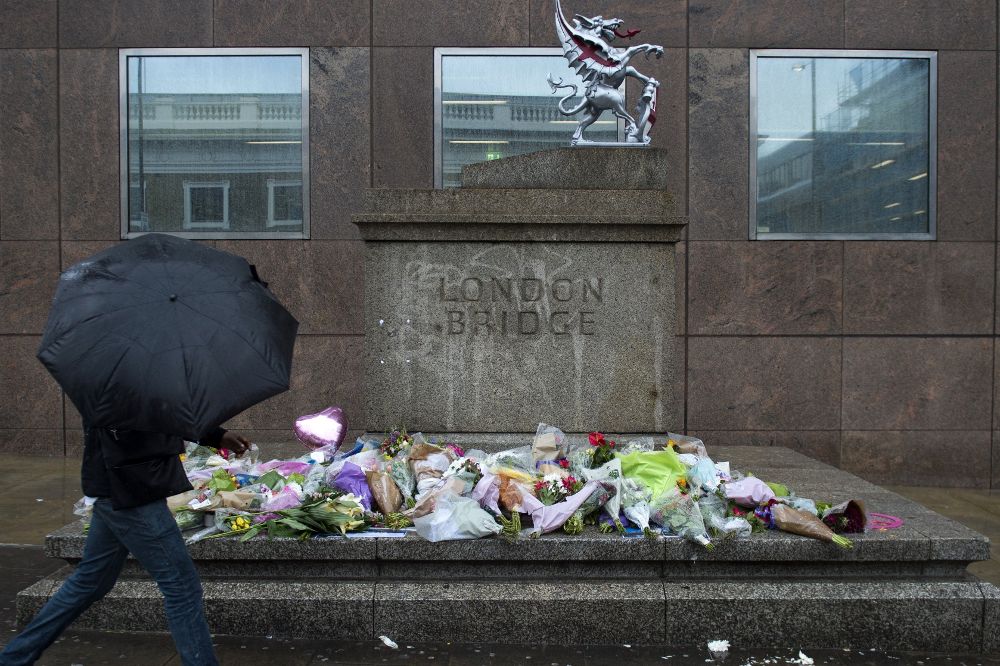 Un viandante pasa delante de varios ramos de flores dejados en memoria de las víctimas en el Puente de Londres.